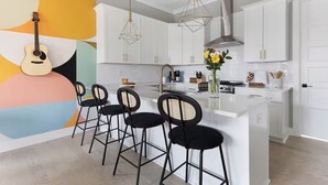 Una cocina moderna con armarios blancos, una isla central con taburetes de bar, luces colgantes y una guitarra en la pared.