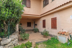 A courtyard with a stone wall, potted plants, and a building with a tiled roof and wooden shutters. - Villa Filippa Pittulongu – Cozy Holiday Home Near the Sea for 4 Guests (Pittulongu)