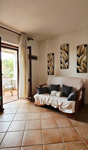 A cozy room with a sofa, a chair, a cross, and leaf-patterned artwork. - Villa Filippa Pittulongu – Cozy Holiday Home Near the Sea for 4 Guests (Pittulongu)