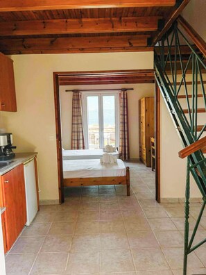 Un dormitorio con una cama de madera, vistas a través de una ventana, una zona de cocina y una escalera.