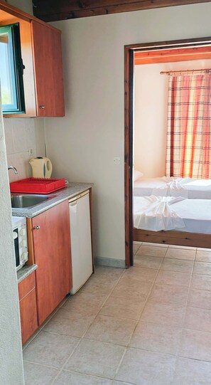Una habitación compacta con kitchenette, una cama y una cortina escocesa, y suelo de baldosas.