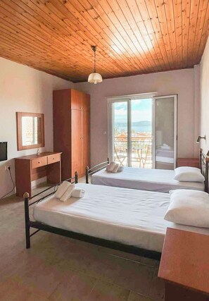 Ein Schlafzimmer mit Holzboden, einem Bett, einem Schreibtisch, einem Kleiderschrank und einem Balkon mit Blick.