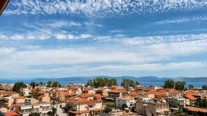 Eine Küstenstadt mit roten Dächern, strahlend blauem Himmel und Blick auf das Meer und die fernen Berge.