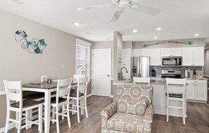 A modern kitchen with white cabinets, a microwave, and a stove. There is a dining area with a table and chairs, and a patterned armchair. - Updated 2 BR 2 BA Unit - 1/2 Block from the Beach (Ocean City)