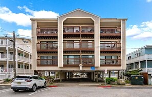 A multi-story hotel with balconies, a parking lot, and a clear sky. - Updated 2 BR 2 BA Unit - 1/2 Block from the Beach (Ocean City)