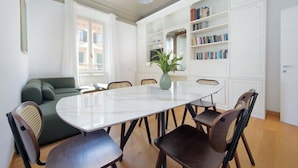 Een eetgedeelte met een ronde tafel, stoelen, een bank en een boekenkast.