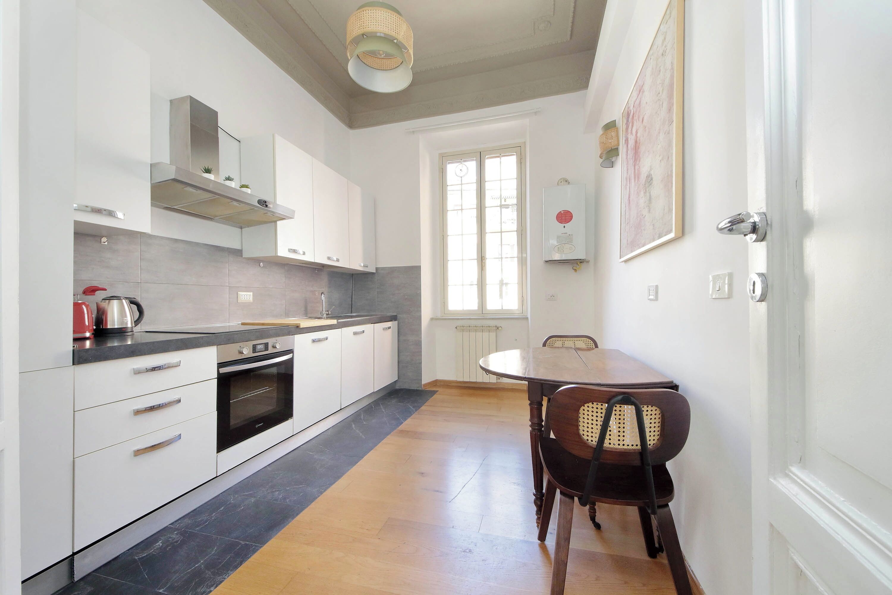 A modern kitchen with white cabinets, a black countertop, and a wooden dining table with a chair.