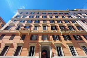 A multi-story building with a symmetrical facade, large windows, and a central entrance with an archway. - Italianway Collection - Casa Tibullo (Rome)