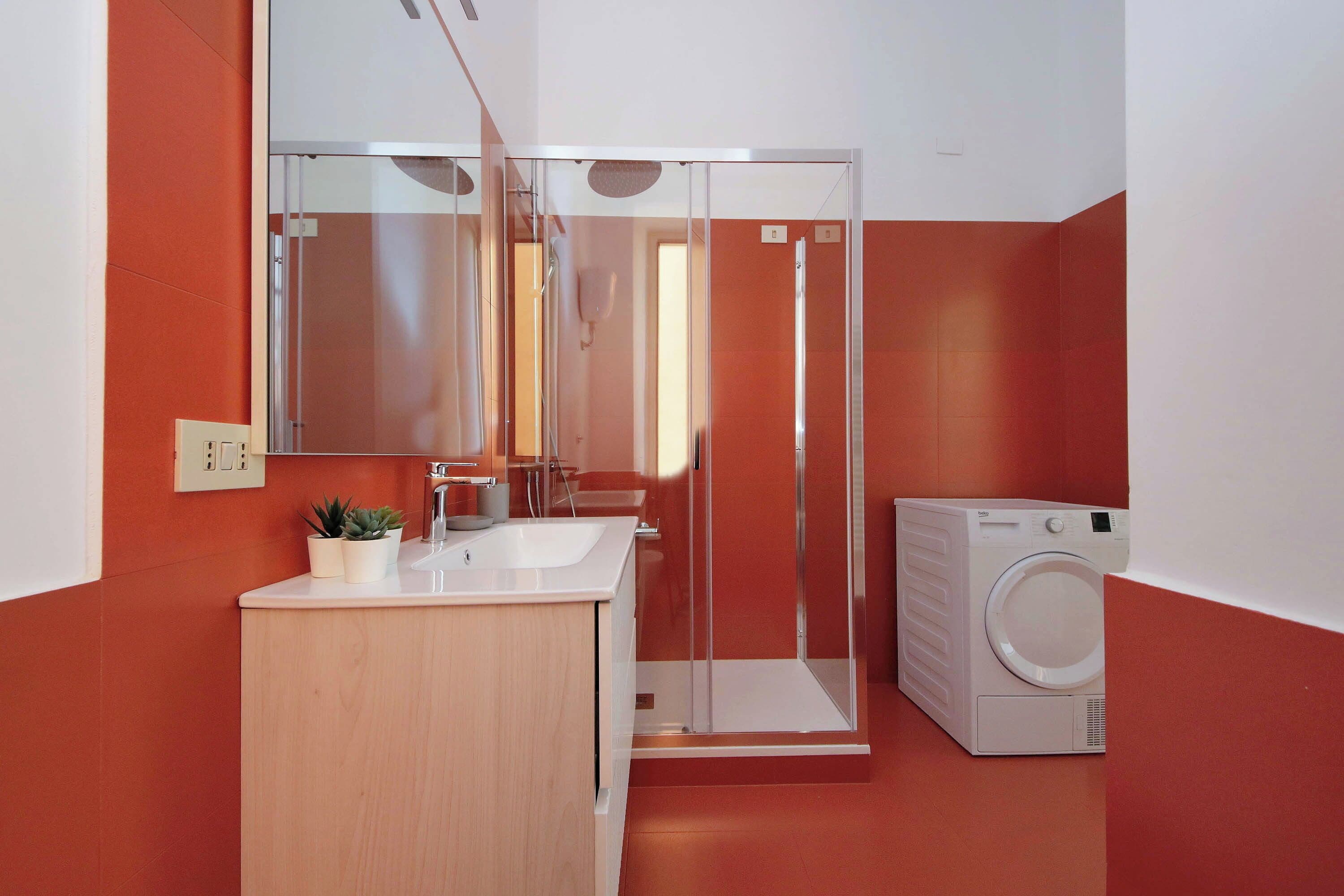 Un baño moderno con cabina de ducha de vidrio, un lavabo con espejo y lavadora integrada.