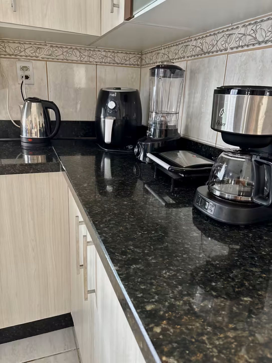A kitchen with a coffee maker, a blender, and a kettle on a granite countertop.