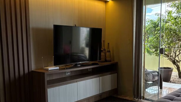 Una sala de estar moderna con una televisión de pantalla plana, un sofá, una mesa de centro y una puerta corrediza de vidrio que da a un espacio al aire libre.