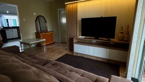 Una sala de estar con un amplio sofá seccional, un televisor de pantalla plana, un mueble de entretenimiento de madera y un ventilador de techo.