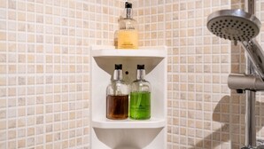 Et badeværelse med bruseniche, hylde med toiletartikler og flisebeklædt væg.