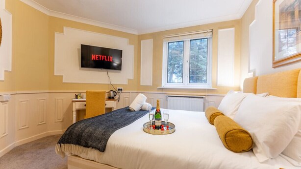 Et hotelværelse med en seng, et tv monteret på væggen, et vindue og et lille skrivebord med stol.