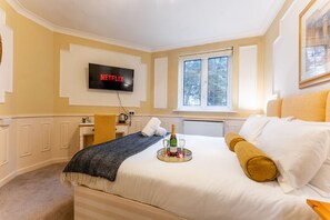 Ett hotellrum med en säng, en tv som är monterad på väggen, ett fönster och ett litet skrivbord med en stol.