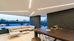 A modern outdoor seating area with a sofa, coffee table, and dining table, featuring a stone wall and a view of the outdoors. - Luxury Villa Asper with Pool and Jacuzzi (Ližnjan)