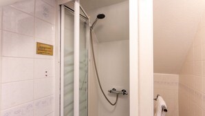 A shower with a glass door, a towel rack, and a sign on the wall.