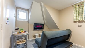 A small room with a sofa, a TV displaying 'NETFLIX,' a small table with food and drinks, and a window. - Cransley Room 11 - Apartment close to the beach with communal garden (Bournemouth)