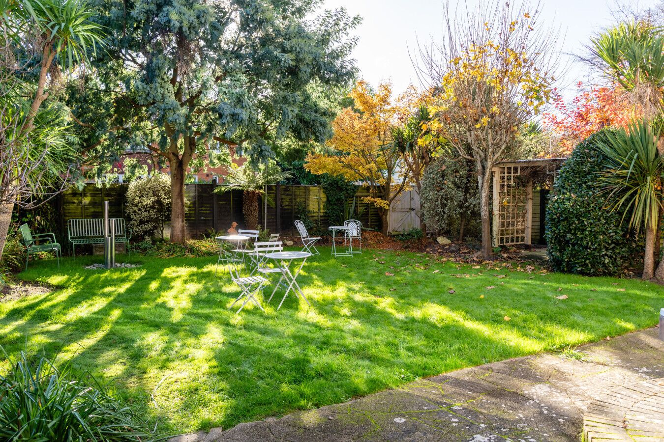Ein gepflegter Garten mit Rasen, einem Metalltisch und Stühlen sowie verschiedenen Bäumen und Sträuchern.