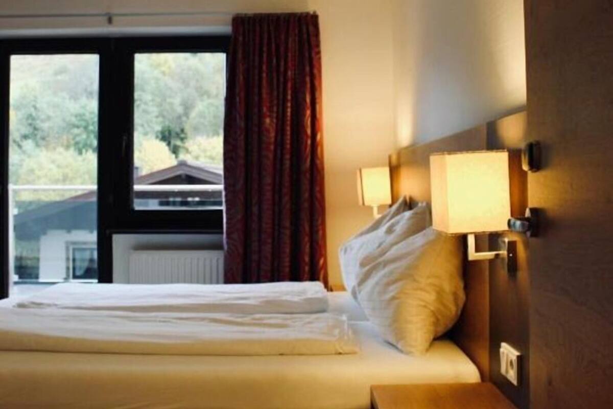 Ein Hotelzimmer mit Bett, einem Vorhangfenster, einer Nachttischlampe und Blick auf Grün.