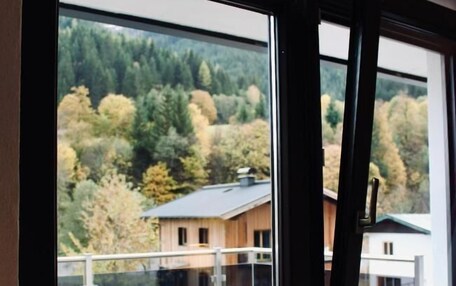 A view from a balcony with a wooden deck, overlooking a forested area and a building with a sloped roof.