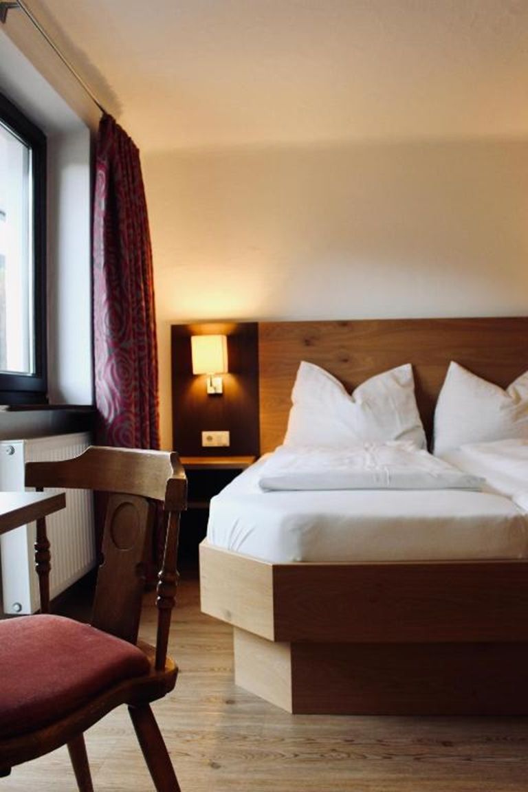 A hotel room with a wooden bed, a desk, a chair, a lamp, and a window with curtains.