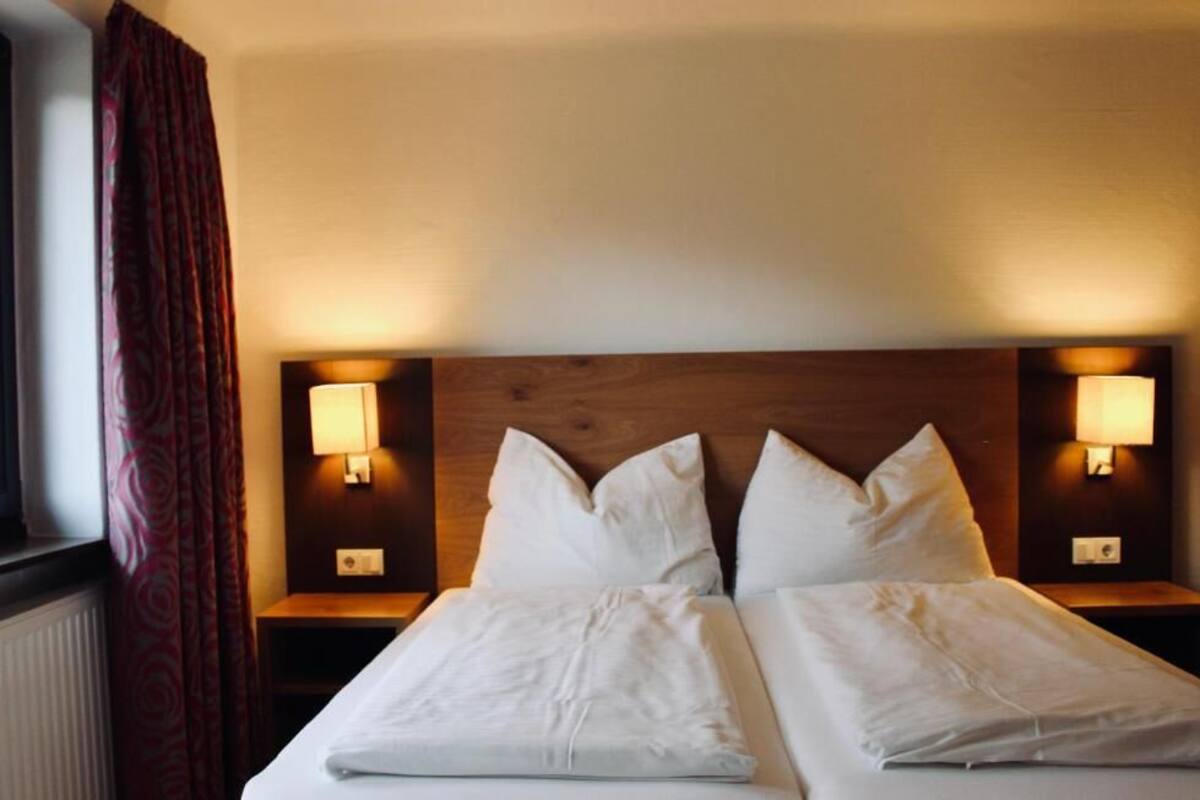 Ein Doppelbett mit weißer Bettwäsche, zwei Nachttische mit Lampen und ein Fenster mit Vorhängen.