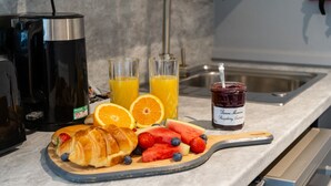 Colazione con croissant, fragole, mirtilli, arance e un vasetto di marmellata su un tagliere di legno.