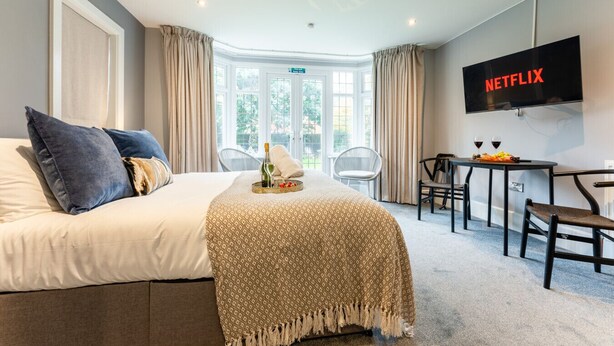 Ein Hotelzimmer mit Bett, Fernseher, Esstisch mit Stühlen und Blick ins Freie.