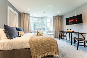 Una habitación de hotel con cama, televisión, mesa de comedor con sillas y vistas al exterior.
