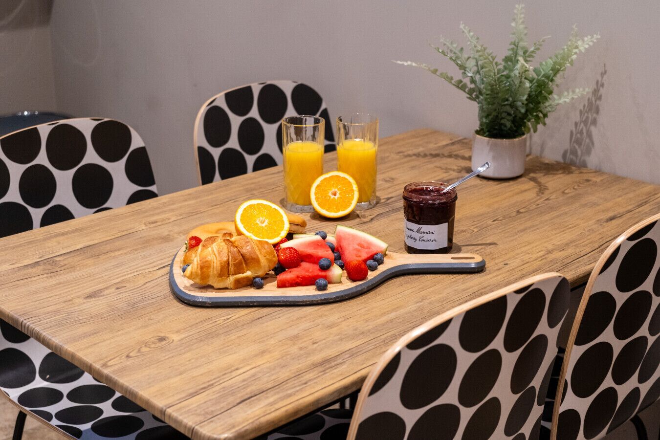 A wooden table with a breakfast setting including croissants, fruits, and a jar of jam.