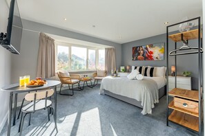 Una habitación de hotel moderna con cama, zona de comedor con sillas, una mesa con desayuno y un ventanal grande.
