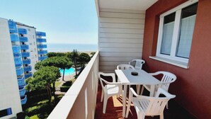 A balcony with a table and chairs, overlooking a pool and buildings. - Seaside Accommodation With Terrace (Lignano Sabbiadoro)