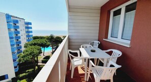 A balcony with a table and chairs, overlooking a pool and buildings. - Seaside Accommodation With Terrace (Lignano Sabbiadoro)