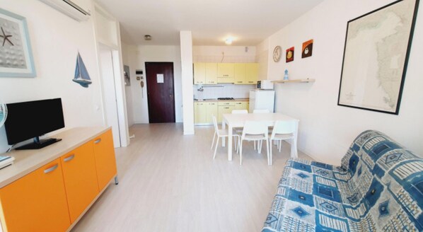 Een woonkamer met een bank, een televisie en een eethoek met stoelen en een tafel.