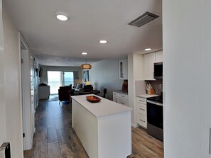Eine moderne Küche mit weißen Schränken, einer zentralen Kochinsel und einem Essbereich mit Sofa und Tisch.