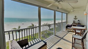 A balcony with a view of the beach, a ceiling fan, and a seating area with a table and chairs. - Pointe South 306 | Modern Gulf Escape + Pool (Fort Myers Beach)