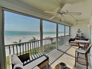 Ein Balkon mit Blick auf den Strand, einem Deckenventilator und einer Sitzecke mit Tisch und Stühlen.