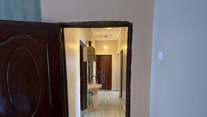 Un corridoio con una porta in legno, pavimento piastrellato e vista su una stanza con lavandino e mobili.