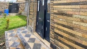 Un edificio con facciata in pietra, due porte nere, un piccolo giardino e un ingresso pavimentato.