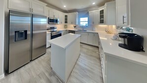 A modern kitchen with stainless steel appliances, white cabinetry, and a central island. - Prince Paradise | Spacious, Gulf Views, + Community Pool (Galveston)