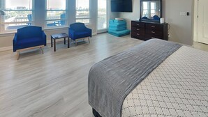 A bedroom with a bed, two chairs, a dresser, a TV, and large windows. - Prince Paradise | Spacious, Gulf Views, + Community Pool (Galveston)