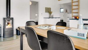 Ett modernt kök med en vedspis, en matplats med ett träbord och stolar samt en köksbänk med en fruktskål.