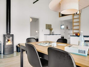 Eine moderne Küche mit Kaminofen, einem Essbereich mit Holztisch und Stühlen sowie einer Küchenarbeitsplatte mit Obstschale.