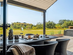 An outdoor dining area with a view of a grassy backyard, a wooden deck, and a house with a slide and swing set. - 4 Star Holiday Home in Saltum (Lokken)