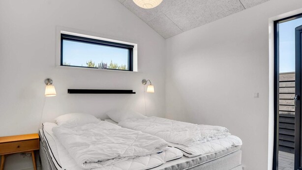 Ett modernt sovrum med en säng, sänglampor, ett fönster och utsikt över grönområden.