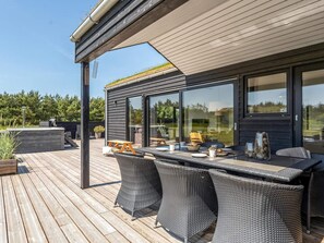 A modern outdoor dining area with a wooden deck, black wicker furniture, and a glass-enclosed space. - 4 Star Holiday Home in Saltum (Lokken)