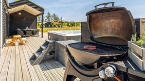 En grill med ett stek på, en träveranda och en liten utomhusplats med ett bord och stolar.