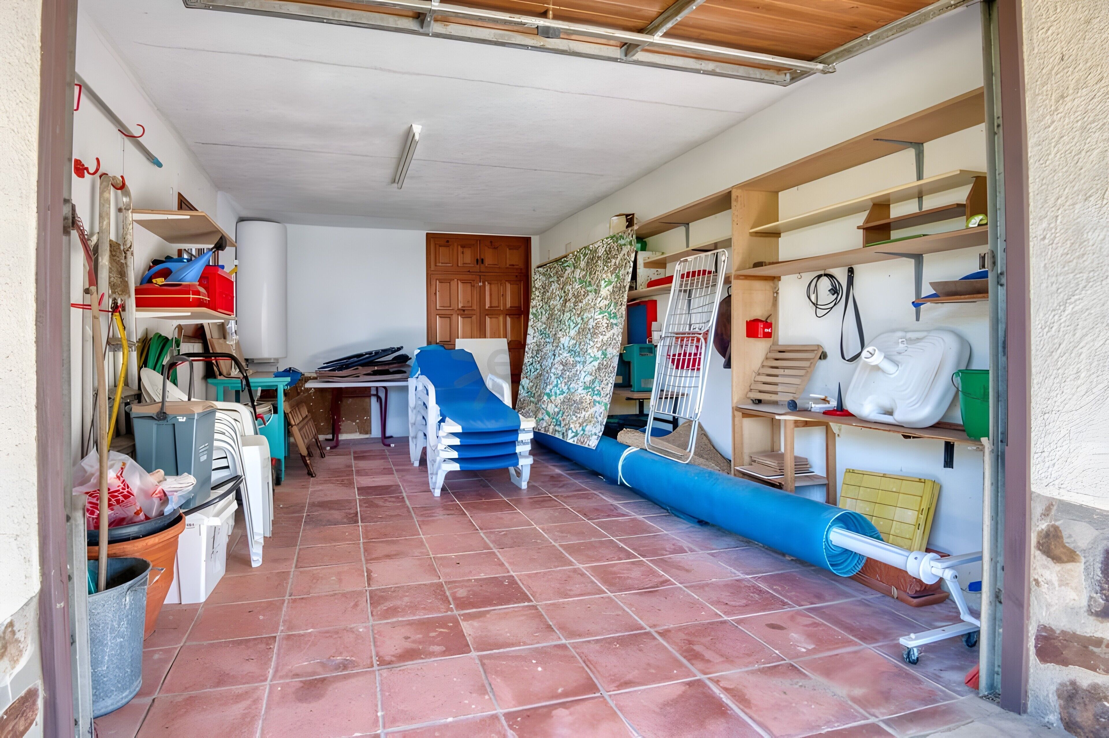 Une pièce avec un sol carrelé, une porte en bois et des étagères remplies de divers objets.
