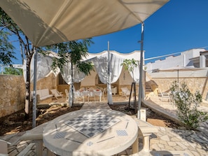 An outdoor seating area with tables and chairs, a round table with a patterned tabletop, and a covered section with white curtains.